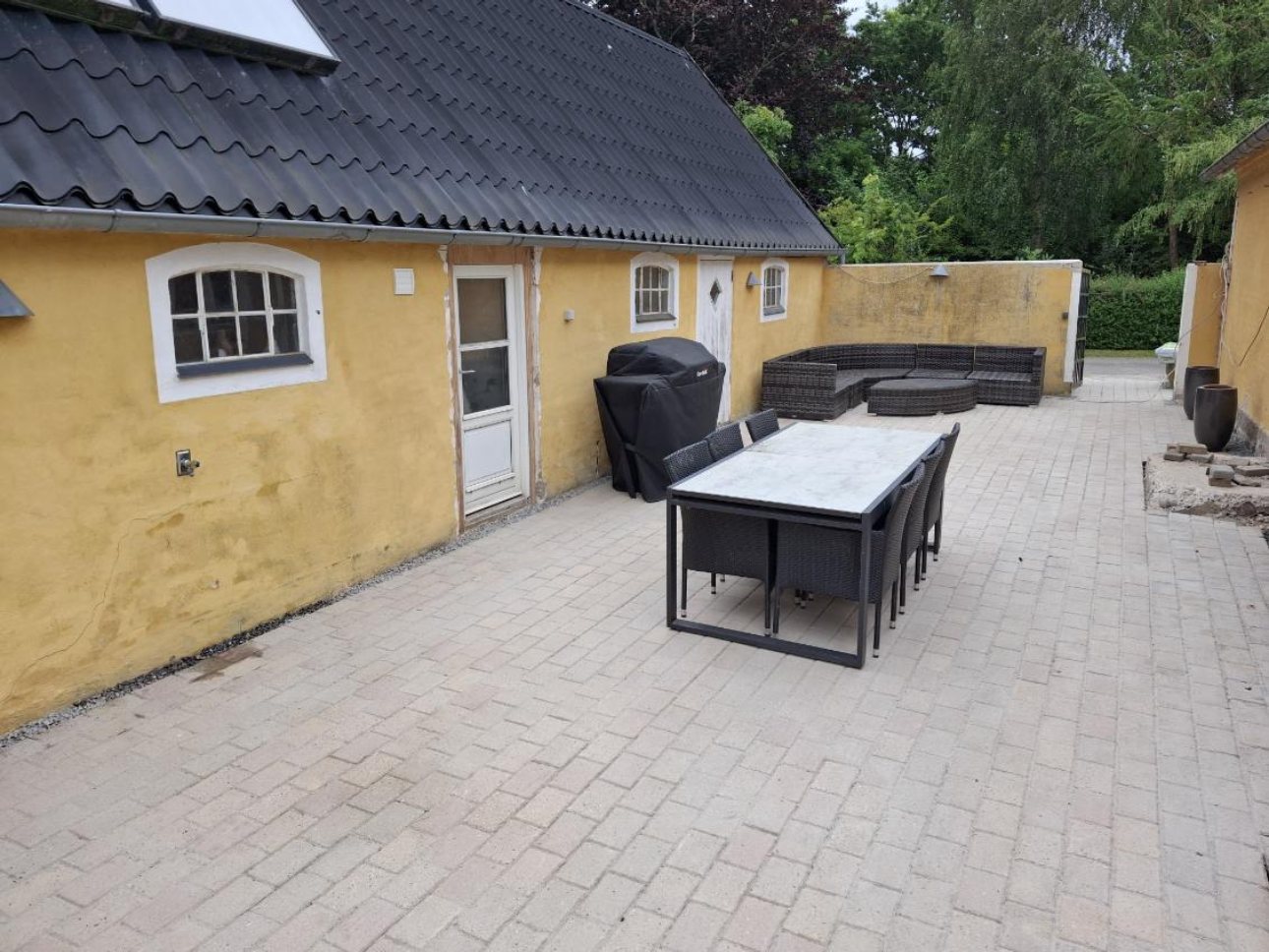 Ny terrasse med belægningssten ved gult stuehus